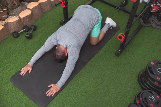istock A fit asian man performs a variant of thoracic extension stretch on a black mat, back arched downwards and arms reached forward. Warming up before a workout at his home gym. 2158547356