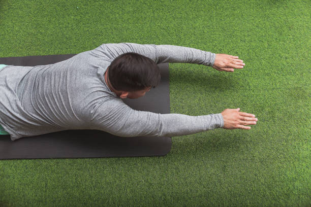 istock A fit asian man does Superman Back Extensions on a black mat. Isometric exercise. Working out and training lower back muscles at a home gym. 2158547360