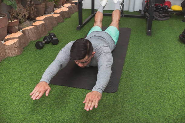 A fit asian man does Superman Back Extensions on a black mat. Isometric exercise. Working out and training lower back muscles at a home gym.