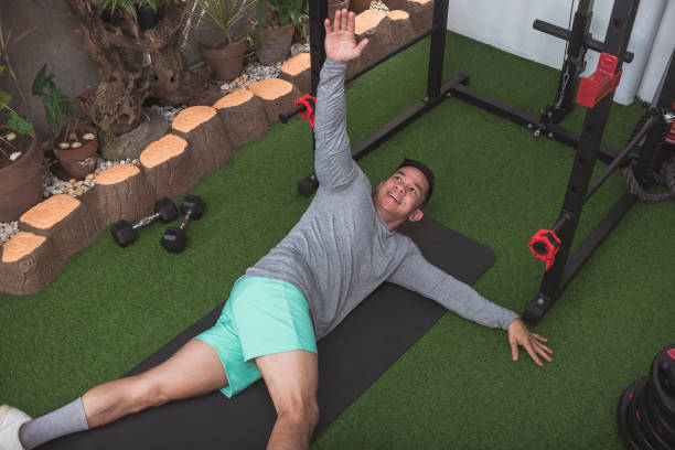 istock A fit asian man in a gray sweater stretches with one arm raised while lying on his side on a black mat. Warming up before a workout at his home gym. 2158547373