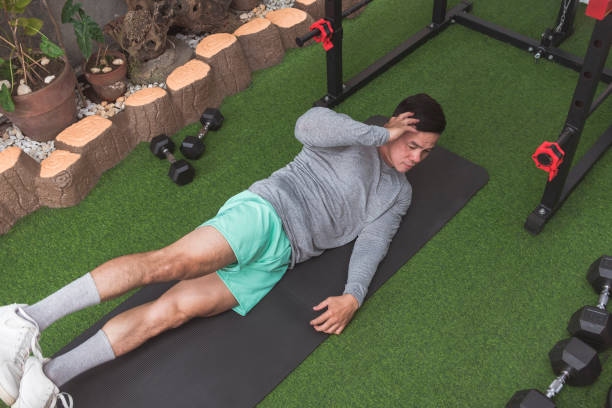 istock An athletic asian man does oblique crunches while lying on a black mat. Leg raised for added challenge. Working out his midsection and core at his home gym. 2158547386