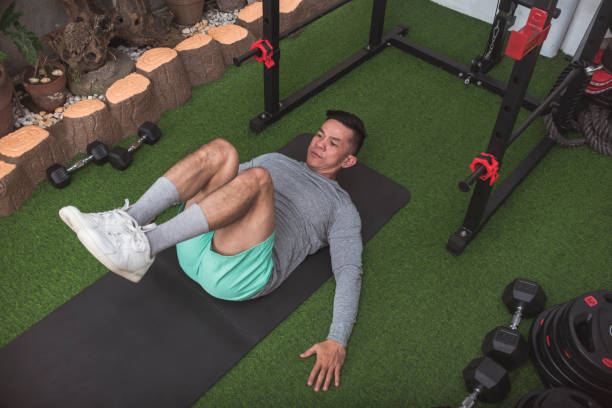 istock A fit asian man does reverse abdominal crunches while lying on a black mat. Working out his core at his home gym. 2158547395