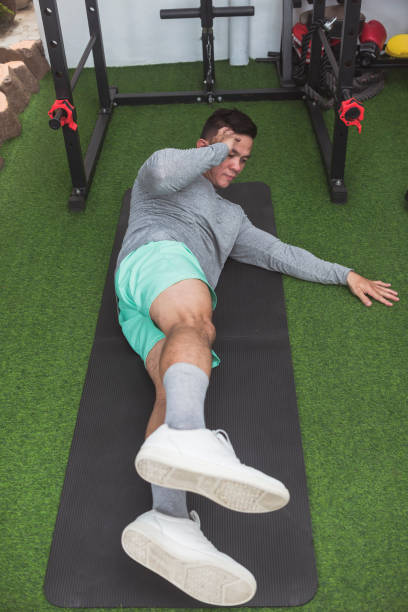 istock A fit asian guy does oblique crunches while lying on a black mat. Leg raised for added challenge. Working out his midsection and core at his home gym. 2158547413