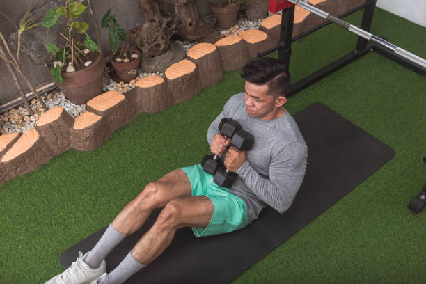 istock A fit asian guy sitting down on a black mat with two hex dumbbells. Starting position for dumbbell cross punches. At a home gym. 2158547483