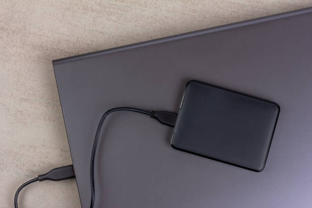 istock a closed laptop with a hard drive connected by a cable close-up on a gray background top view 2158547531