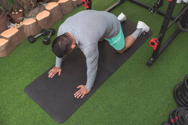 istock A fit asian man in a gray sweater performs a cat stretch with back arched on a black mat. Warming up before a workout at his home gym. 2158547586