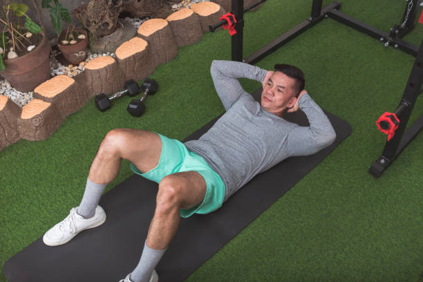 istock A fit asian man in a gray sweater performs a crunches on a black mat. Working out abs at his home gym. 2158547608