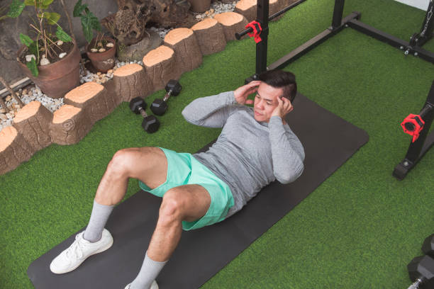 istock A fit asian man does abdominal crunches while lying on a black mat. Working out his core at his home gym. 2158547609