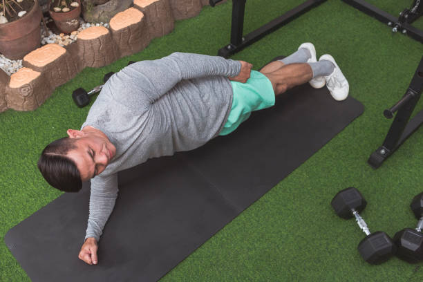 istock A fit asian man performs side planks on a black mat. Core workout at his home gym. 2158547618