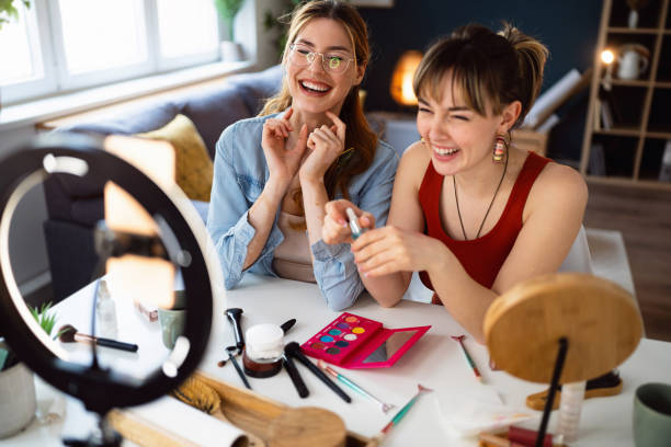 Two young women, influencers, recording a make-up tutorial for their vlog.