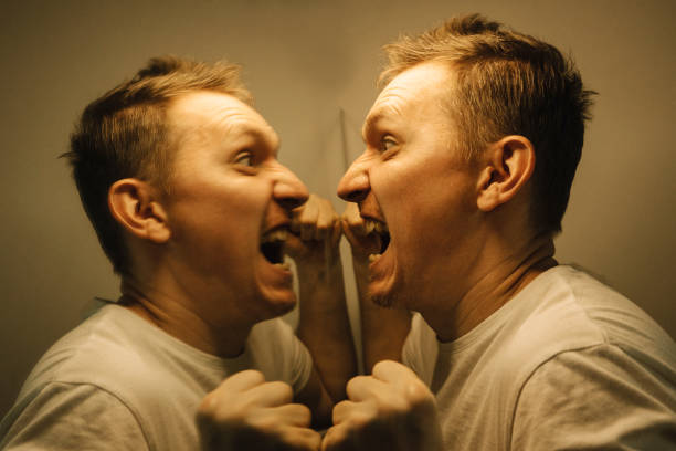 A distraught man in a white T-shirt screams at his reflection in the mirror. Flesh brown tint. Crazy man hits a mirror. Close-up. High quality photo
