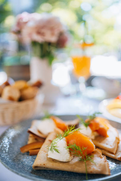 Close-up of a beautifully decorated restaurant table with salmon pancakes, fruit salad and dessert.