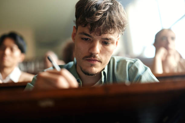 istock Young male student writing an exam in lecture hall. 2158554944
