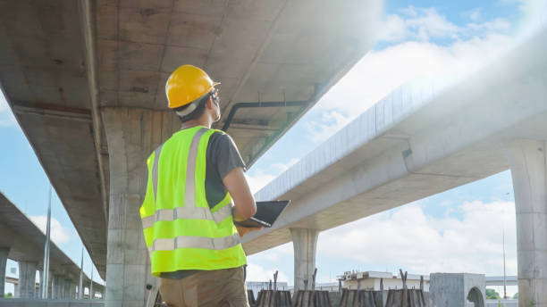 Asian construction supervisor wearing a laptop inspects construction work highway road bridge