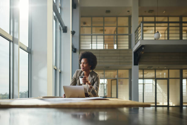 Black female entrepreneur drinking coffee while working on laptop in the building.