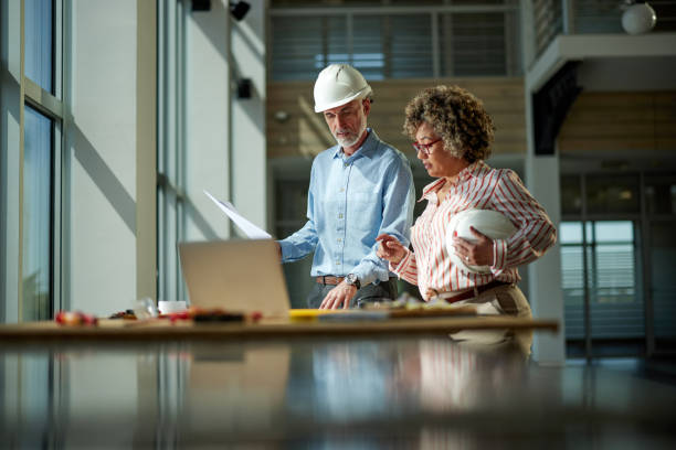 two architects working on plans at construction site. - bouwplaats stockfoto's en -beelden