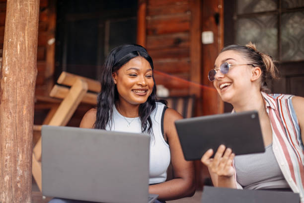 istock Young female friends spending weekend together at cottage house on balcony using wireless technology 2158558403