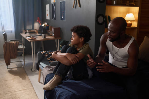 istock Black Man Talking to Depressed Son Sitting on Bed 2158561476