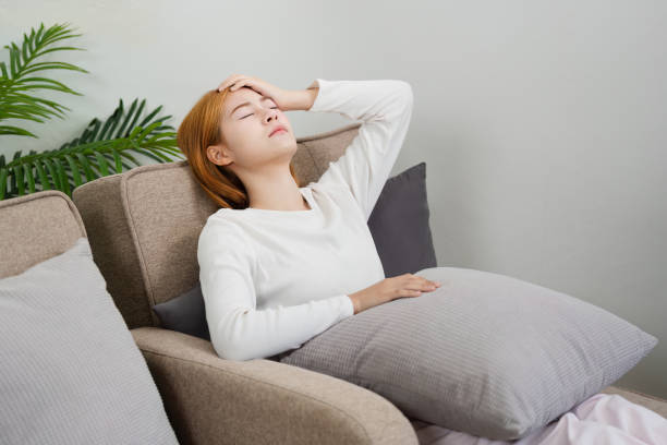 istock Young Woman Feeling Unwell at Home, Resting on Sofa with Hand on Forehead, Experiencing Sickness or Fatigue, Indoor Lifestyle Concept, Cozy Living Room Setting, Health and Wellness Theme 2158563667
