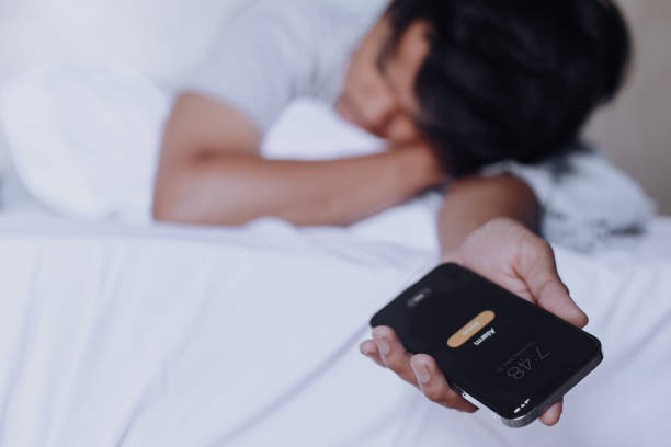 istock Man Sleeping With Alarm Ringing on Smart Phone 2158568537