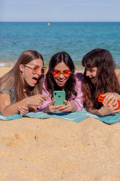 istock Three happy young friends on the beach using apps on their smartphones.Vertical 2158568932