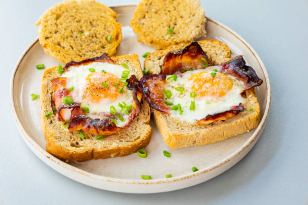 istock Baked Bacon and Eggs in Bread on White Plate with Fresh Green Onion Close-Up 2158570087