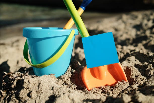 Colorful plastic beach toys are laying on the sand with a blank blue sign for your text