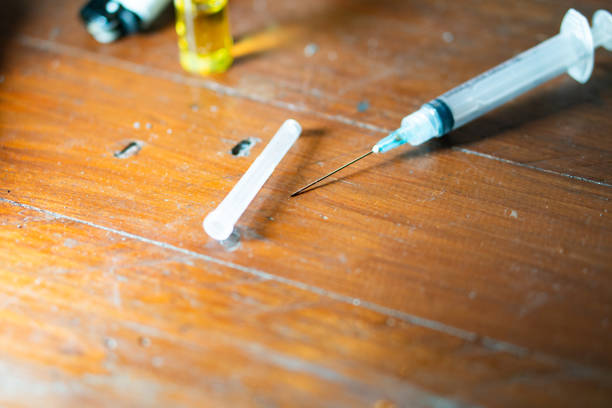 A syringe with a needle and a small vial on a wooden surface, suggesting medical or drug use.