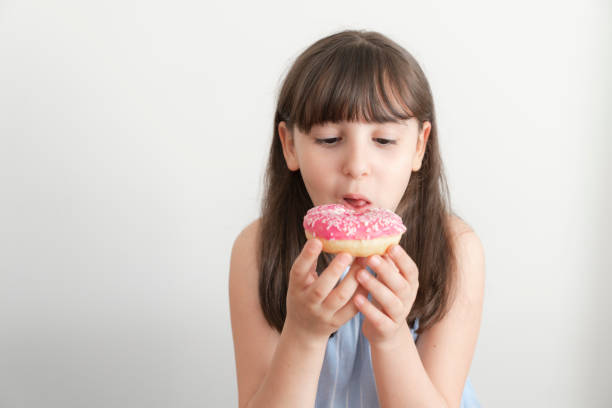istock Little girl is eating pink doughnut 2158575240