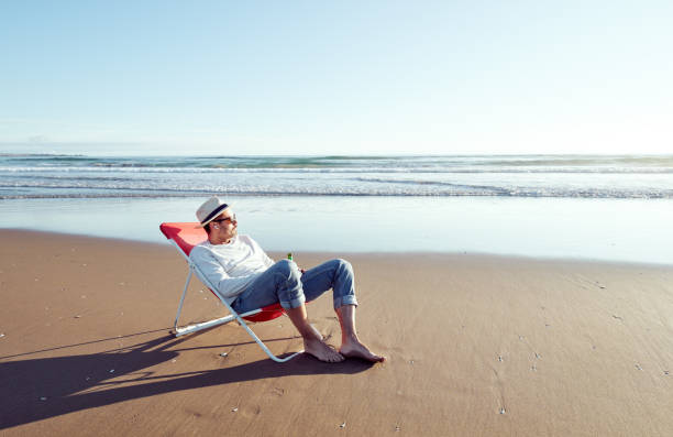 alone mature man lying on beach chair relaxing looking the horizon on the remote beach shore