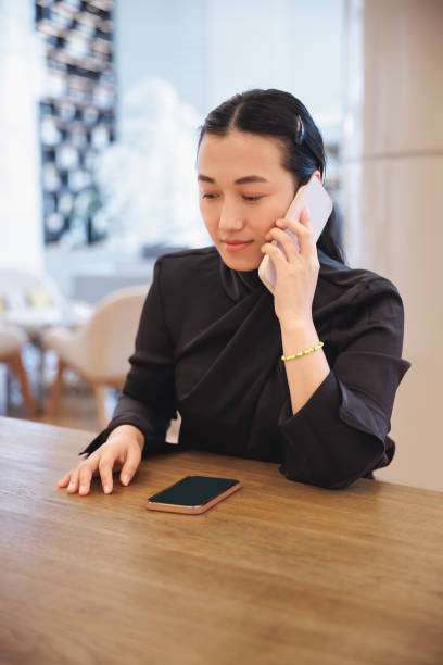 istock Young Asian woman making a call on the phone, her other mobile device on the table 2158578123