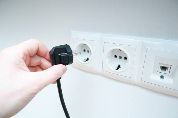 istock A man's hand holds an electrical plug next to the sockets on the white wall. Hand holds electric plug. 2158578236