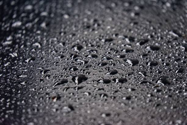 istock Blurred many rain droplets on a black leather with bokeh light and dark background 2158586499