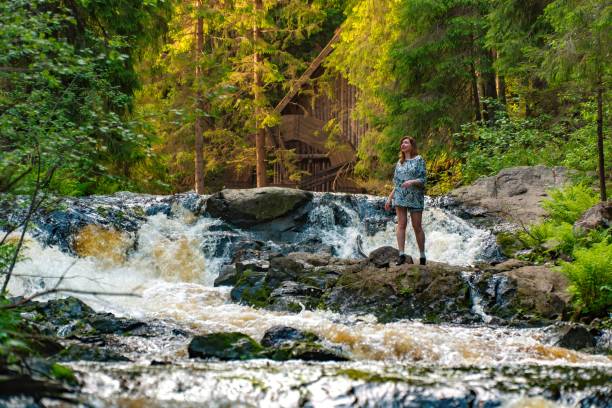 istock Woman Standing on Rocks by a Rushing Waterfall in the Forest 2158602650