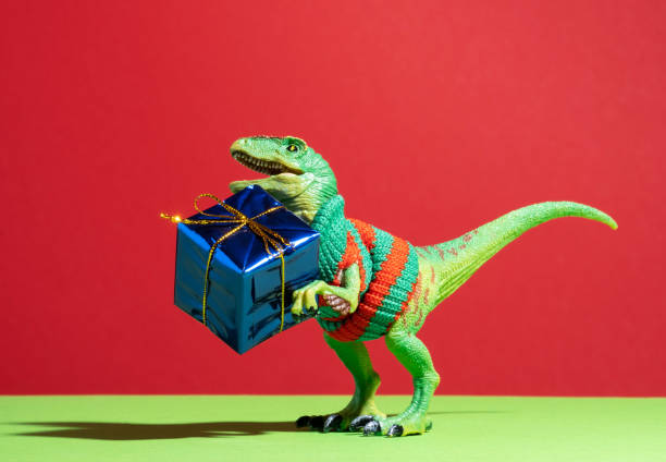 istock Cute dinosaur with blue foil present box on red green background. 2158603070