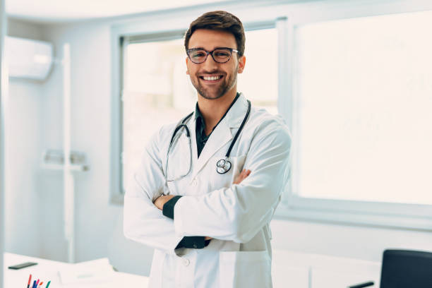 Handsome male doctor with stethoscope over neck working while looking at camera in the medical consultation. Portrait of handsome male doctor with stethoscope over neck working while looking at camera in the medical consultation. doctor stock pictures, royalty-free photos & images