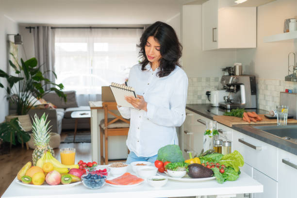 istock Confident middle aged female Indian Nutritionist expert writing diet plan for herself or client, table full of fruits and vegetables. Healthy diet habits and wellness lifestyle, weight loss program. 2158627123
