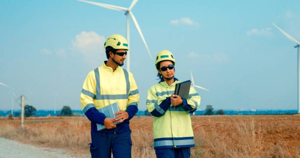 istock Renewable energy engineers walking consult digital tablet while working on maintenance and efficiency of wind turbines in rural. Green ecological power generation wind sustainable energy. 2158629477