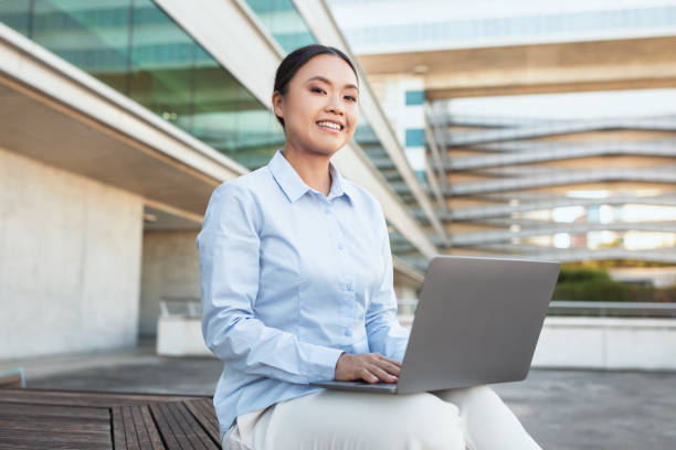 istock Asian Woman Sitting on Bench With Laptop 2158629786