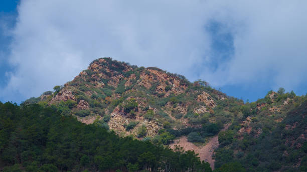 istock A lush green mountain range with rocky outcrops is depicted under a partly cloudy sky. 2158634633
