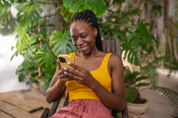 istock Joyful black woman smiling using smartphone relaxing chatting in social media sit among houseplants. 2158642707