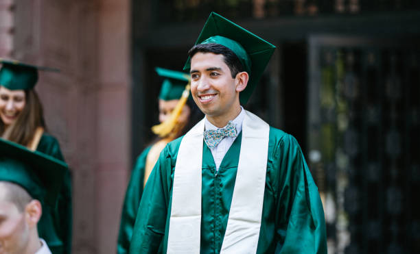 Four cheerful multi-ethnic students wearing graduation gowns and caps gesturing peace sign