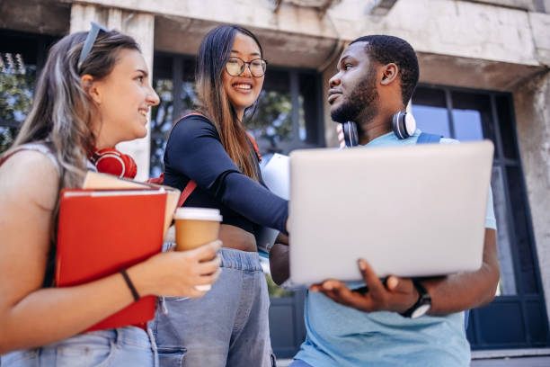 istock Multiracial group of students standing in front of University after class looking at laptop 2158653788