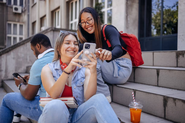 istock Multiracial group of students sitting in front of University after class using mobile phones 2158654021