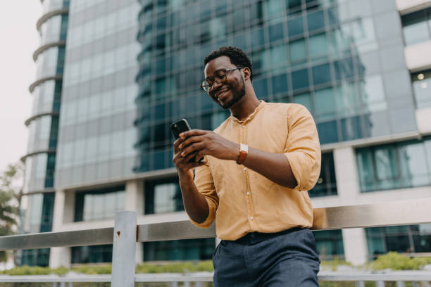 istock Man in yellow shirt using phone against glass building 2158655575