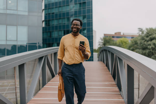 istock Man walking on bridge, smiling at phone in yellow shirt 2158655719