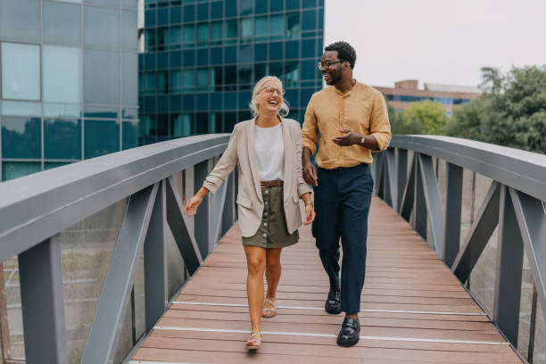 Laughing colleagues walk on bridge in urban scenery.