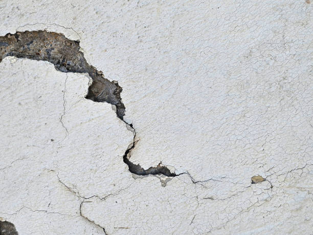 istock textured surface with a prominent, irregular crack. The crack branches out and is surrounded by peeling, flaking off white paint, suggesting material degradation. 2158661118