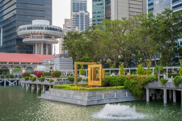 Front of Queen Sirikit National Convention Center in Bangkok at Ratchadaphisek Rd, Khlong Toe. In front of glassy facade  is golden sign. Some thai people are walking in right bottom area. Captured at early sunset time