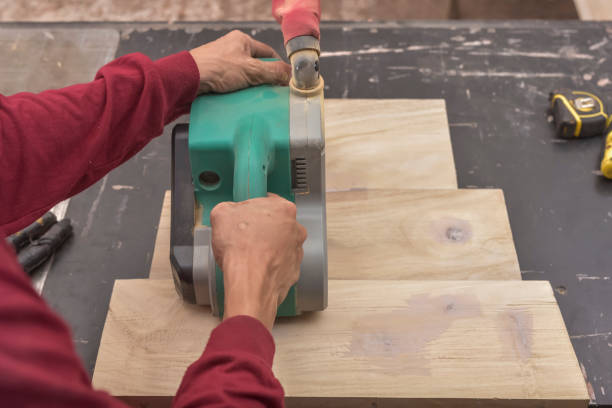 Using a hand-held sanding machine or belt sander to level the surface of a glued wood for a cabinet, table or other furniture at a workshop.